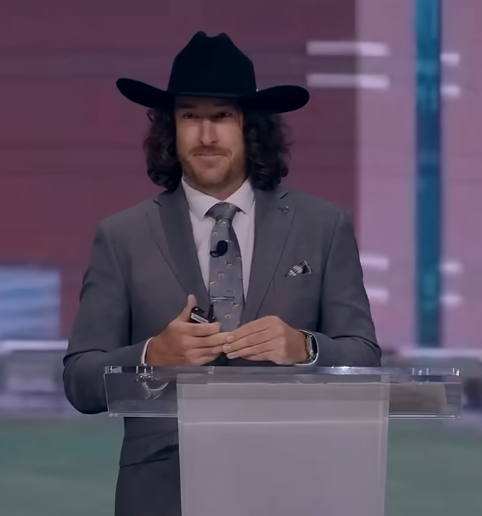 Jeff Zausch net worth success reflected as he delivers a motivational speech on stage wearing a black cowboy hat and gray suit