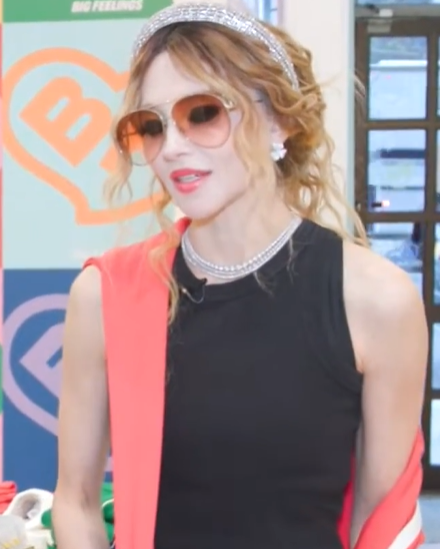 Stacey Bendet, founder of Alice + Olivia, wearing a black sleeveless dress with a coral jacket and jeweled headband at a fashion event, representing her successful career and $200 million net worth.