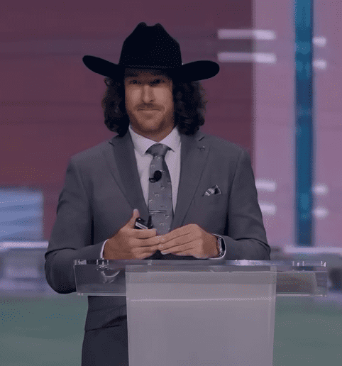 Jeff Zausch net worth success reflected as he delivers a motivational speech on stage wearing a black cowboy hat and gray suit