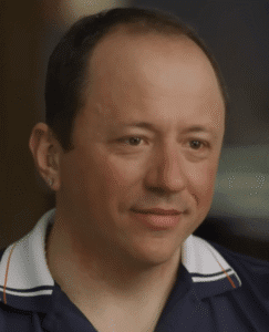 Shane Van Boening close-up portrait wearing a navy collared shirt, smiling during an interview.